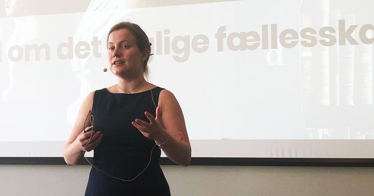 Andrea Plovgaard Frederiksen giving a presentation with a headset microphone in front of a screen displaying Danish text.