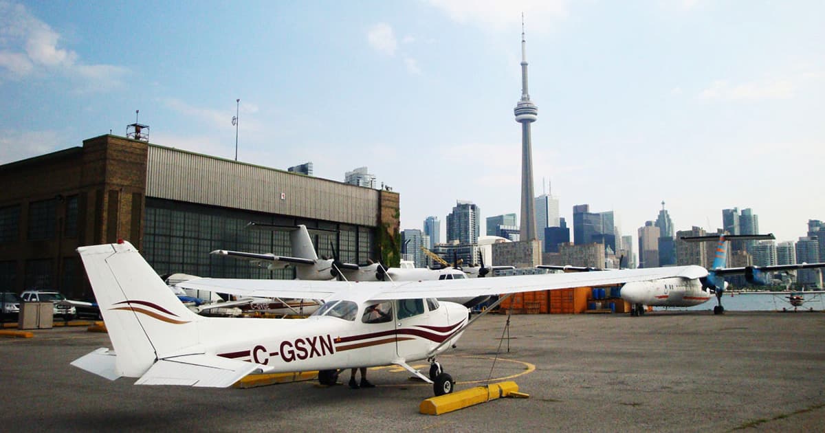 A small aircraft with the registration C-GSXN parked on the tarmac at an airport, with Toronto's CN Tower and skyline visible in the background.