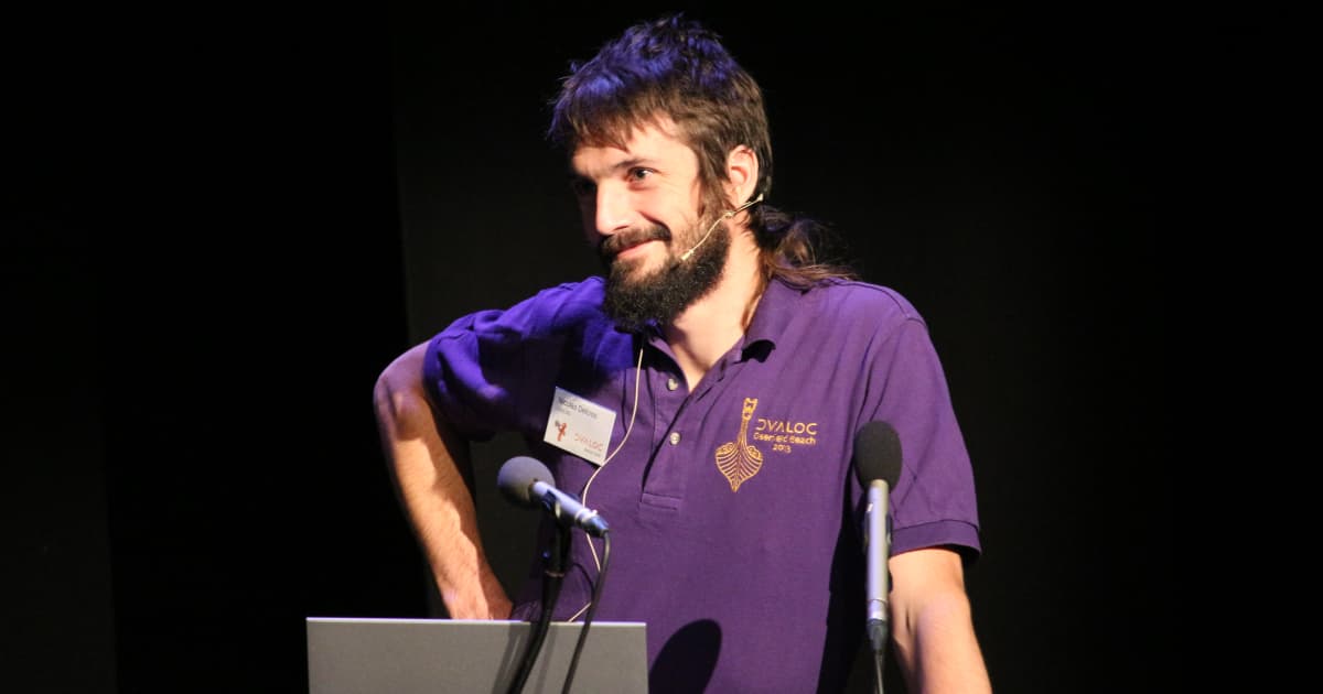 Nicolas Delcros presenting at Dyalog ’18, standing at a podium with microphones, wearing a purple conference shirt and headset microphone.
