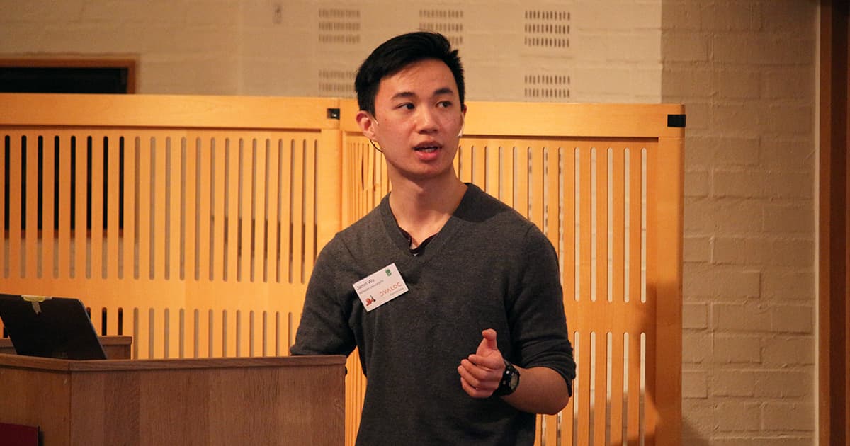 Jamin Wu giving a presentation at Dyalog '19, standing behind a podium and speaking into a headset microphone.