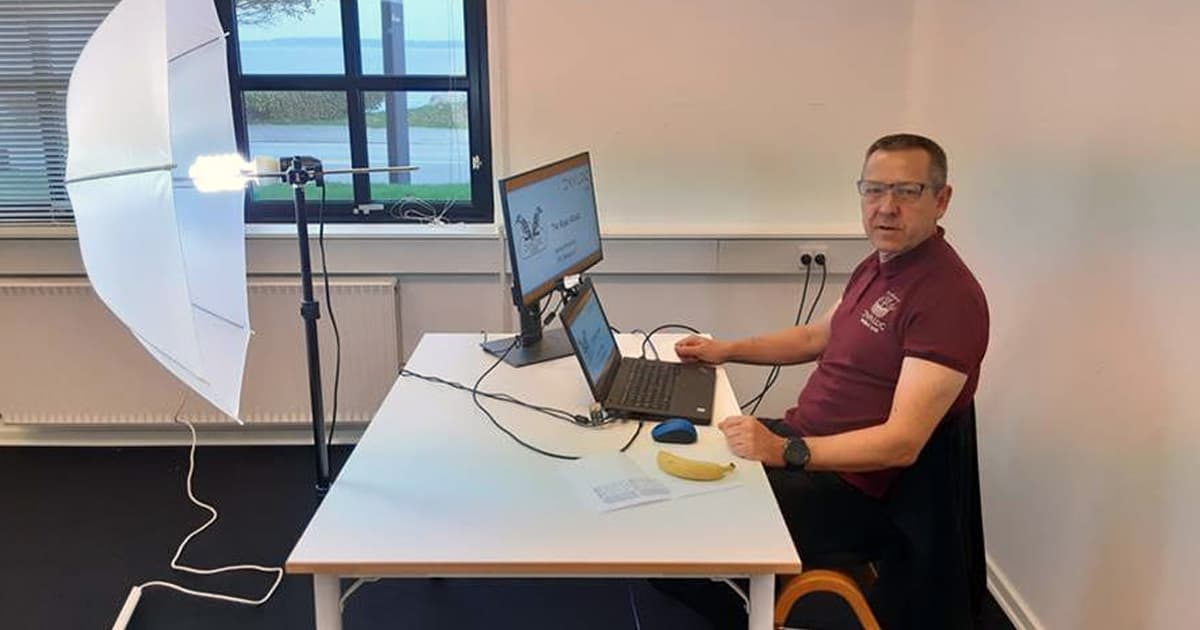 Morten Kromberg seated at a desk with two monitors, preparing a recording with lighting equipment set up, during a Dyalog event.