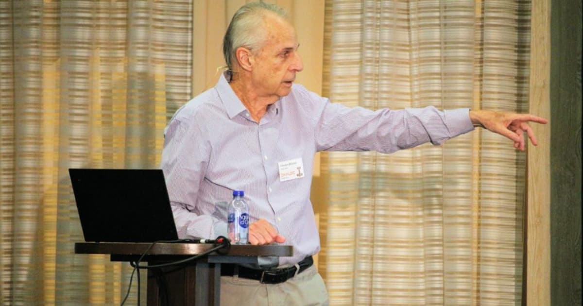 Charles Brenner speaking at Dyalog '22 in Olhão, Portugal, during a presentation on numerical integration, gesturing to the side while standing at a podium with a laptop and water bottle.