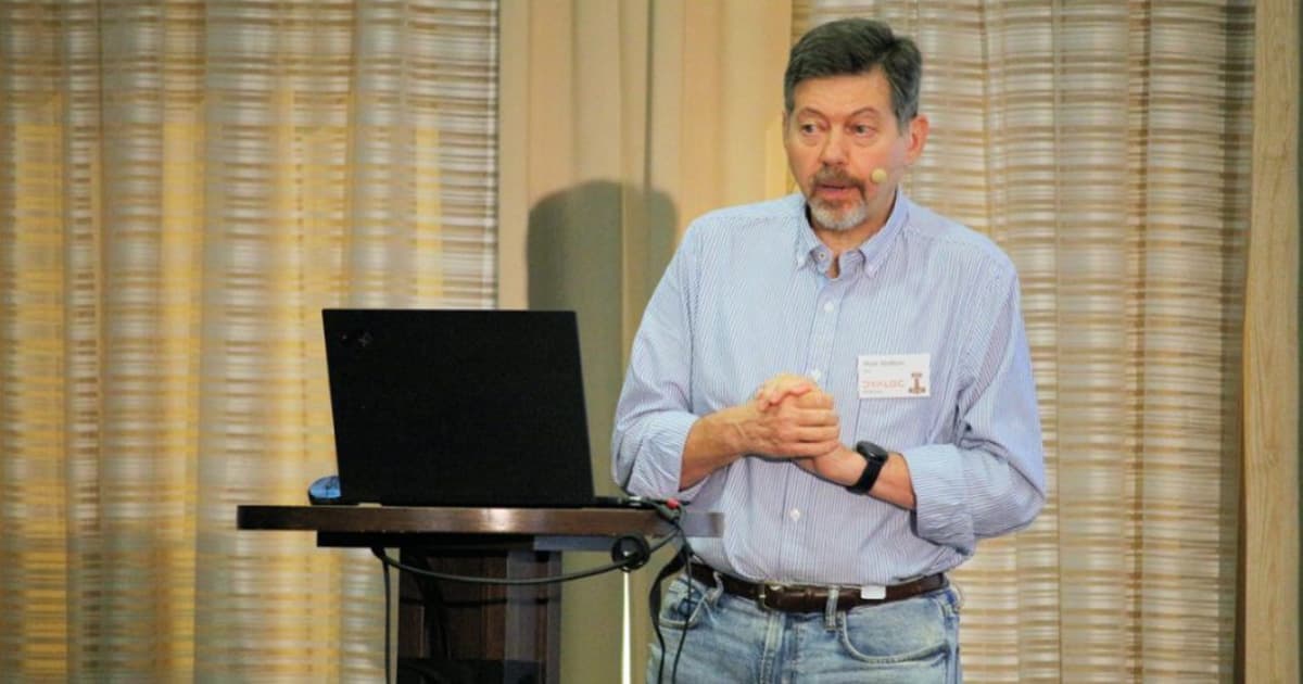 Mark Wolfson speaking at Dyalog '22 in Olhão, Portugal, giving a presentation about the North American jewellery retail industry, standing at a podium with a laptop and wearing a headset microphone.
