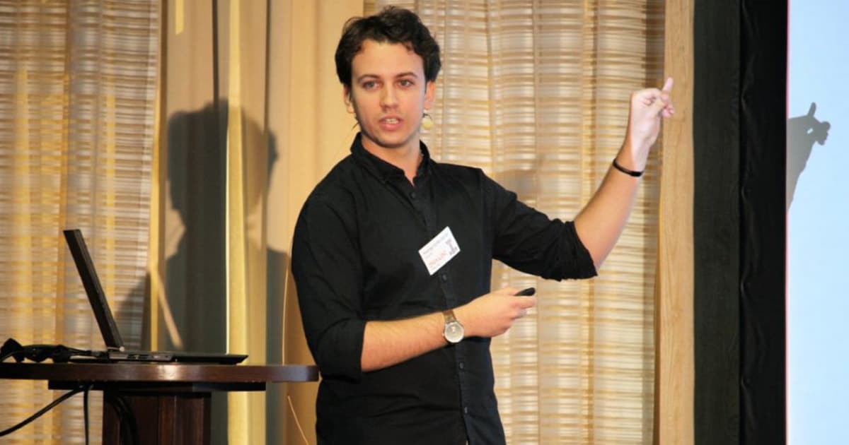 Rodrigo Girão Serrão presenting at Dyalog '22 in Olhão, Portugal, explaining the U-net convolutional neural network (CNN) implemented in APL while gesturing toward the screen.