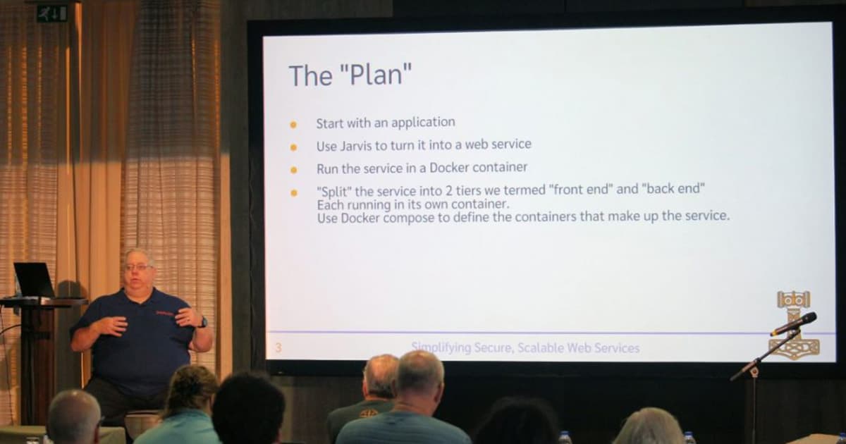Brian Becker presenting at Dyalog '22 in Olhão, Portugal, discussing how to create and deploy web services using Jarvis and Docker, with a slide titled “The Plan” outlining the step-by-step approach.