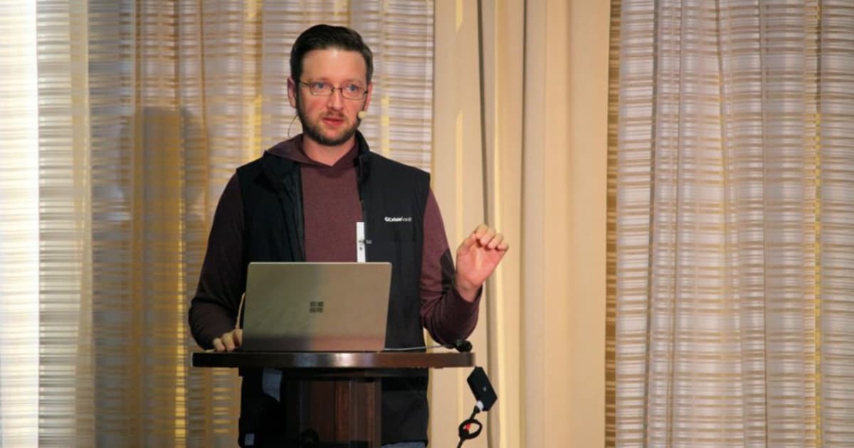 Norbert Jurkiewicz presenting at Dyalog '22 in Olhão, Portugal, sharing his perspective on using the web stack for front-end development while speaking at a podium with a Surface laptop.