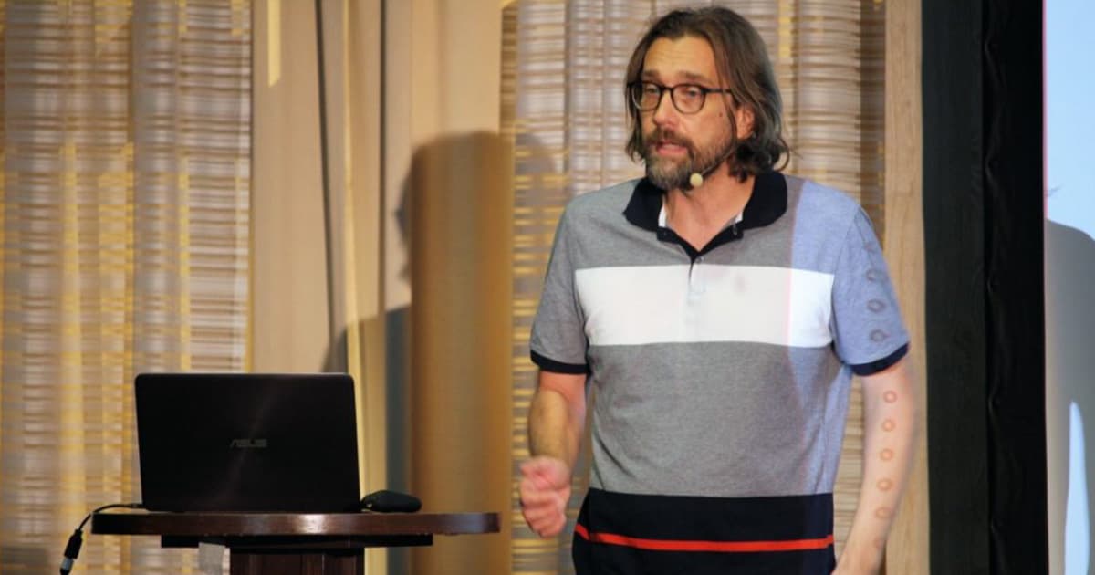 Michael Higginson presenting at Dyalog '22 in Olhão, Portugal, sharing his personal journey into array programming while speaking beside a podium with a laptop.