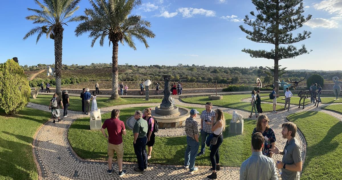 Delegates enjoying the afternoon sun at Quinta dos Vales winery in the Algarve, Portugal, surrounded by sculpture gardens, palm trees, and vineyard views during Dyalog '22.