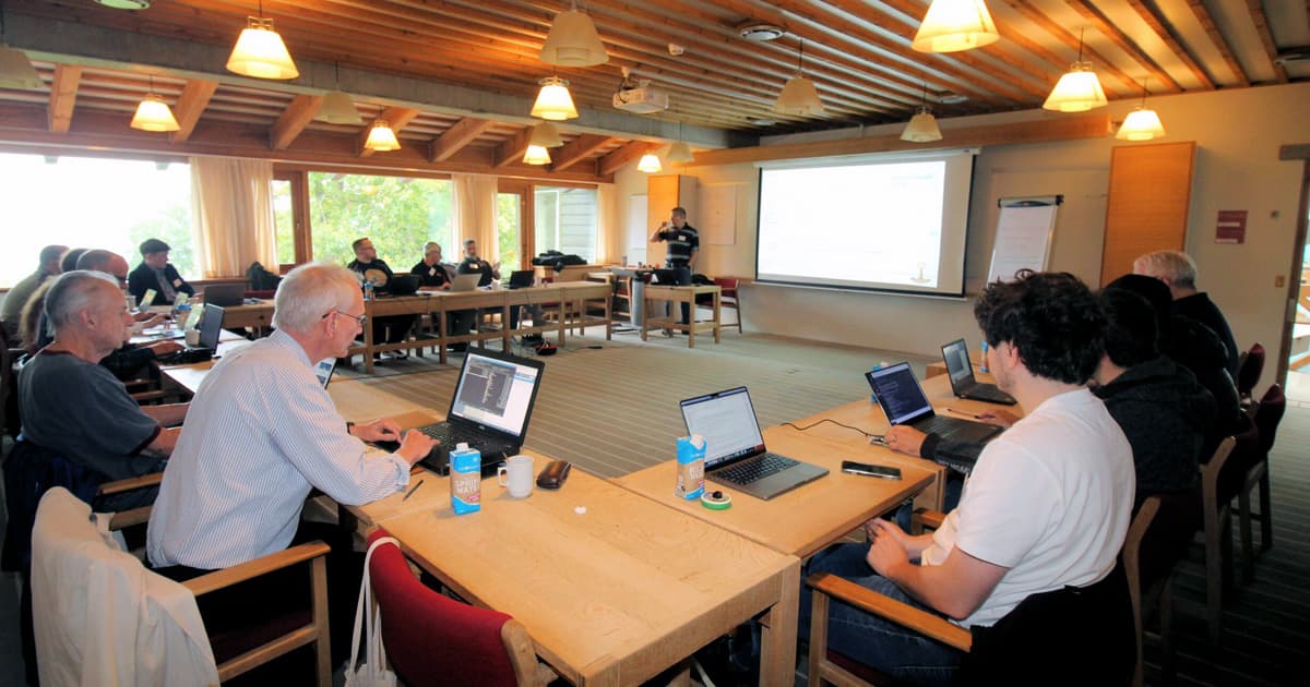 Attendees seated with laptops during a workshop session at Dyalog ’23 in Denmark, with a presenter speaking in front of a projected screen.