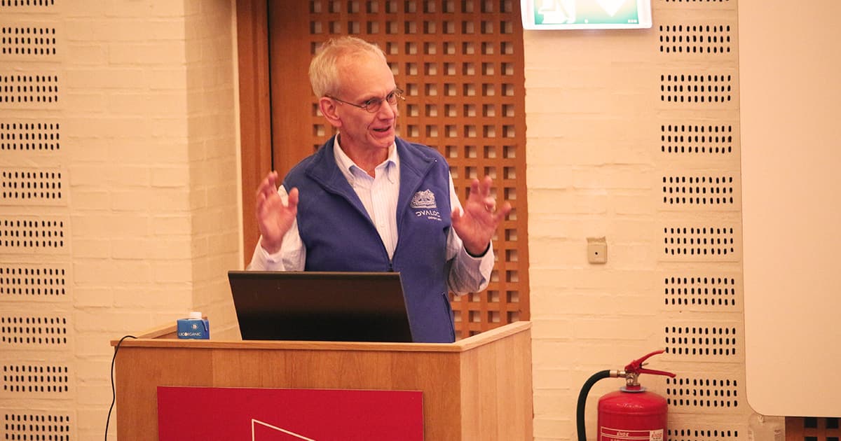 Kai Jaeger presenting at Dyalog ’23, standing at a podium in a blue vest, gesturing with both hands while speaking.