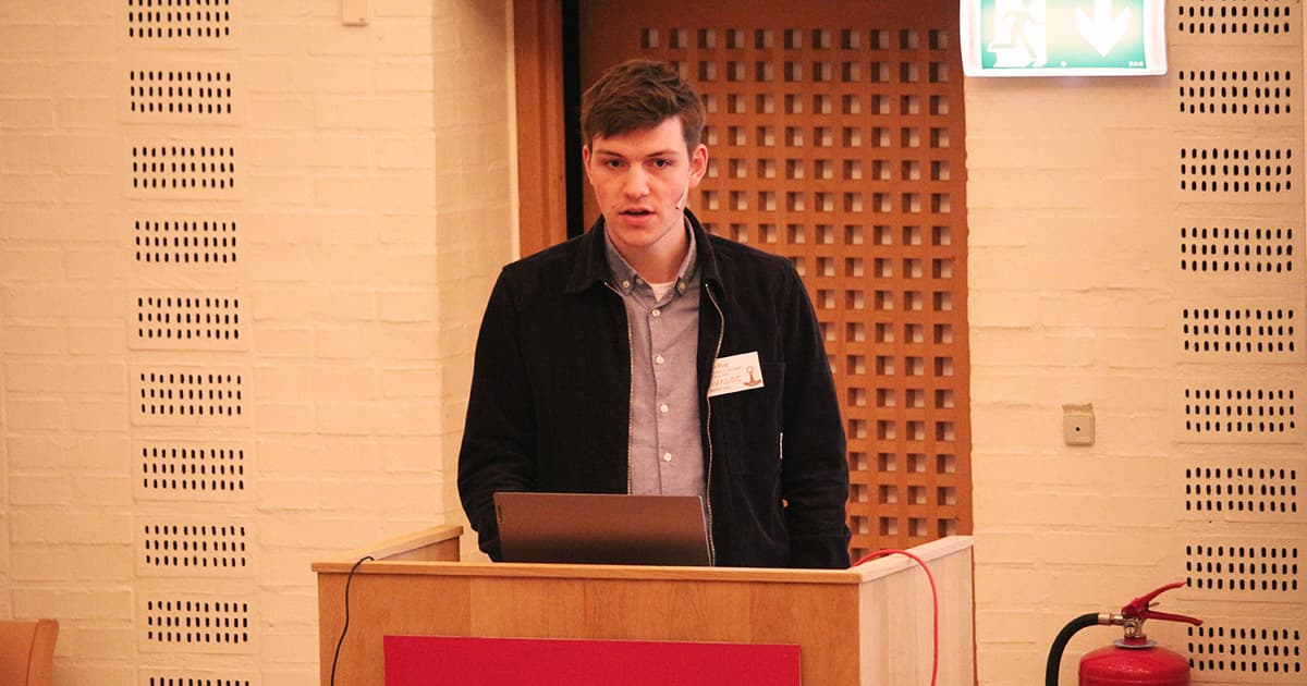 Finn Flug presenting at Dyalog ’23, standing at a podium with a laptop, wearing a dark jacket and light shirt.