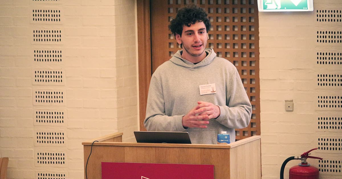 Marcos Frenkel presenting on quantum computing at Dyalog ’23, standing at a podium with a laptop and speaking to the audience.