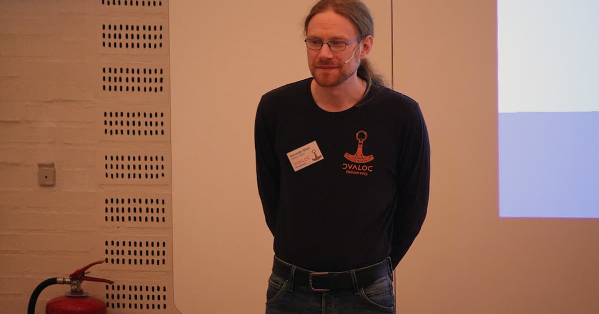 1Alexander Block presenting at Dyalog ’23, standing with hands behind his back, wearing glasses and a dark Dyalog conference shirt.