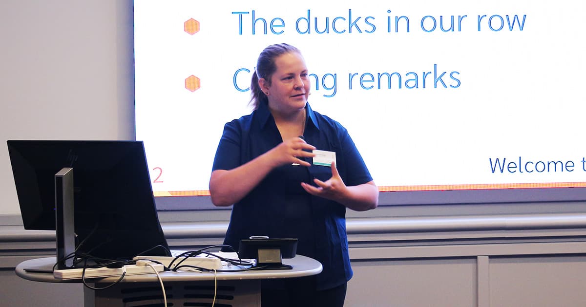 Stine Kromberg, CEO of Dyalog Ltd, delivering the closing remarks at Dyalog ’24 in Glasgow. She stands in front of a presentation slide that reads “The ducks in our row” and “Closing remarks,” gesturing as she speaks.