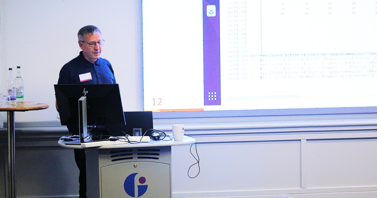 Morten Kromberg stands at a podium during his Dyalog ’24 presentation, with slides projected on the screen behind him.