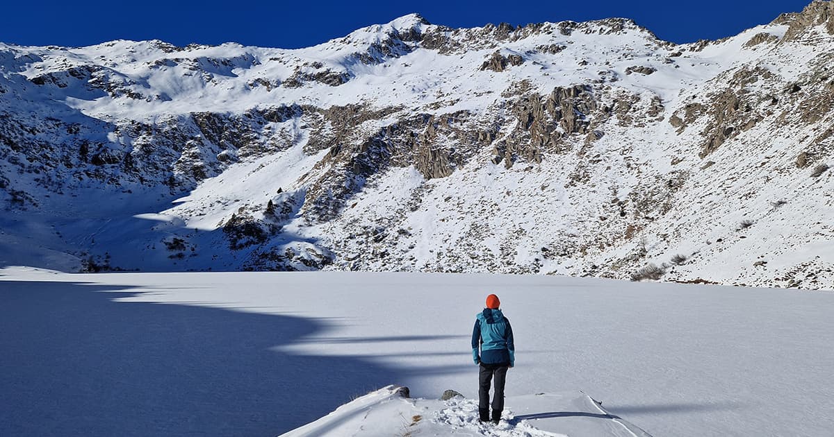 Martina Crippa stands on a snowy ridge, overlooking a frozen lake and snow-covered mountains.