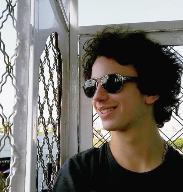 Rodrigo Girão Serrão smiling and wearing sunglasses while looking out from a metal-framed structure.