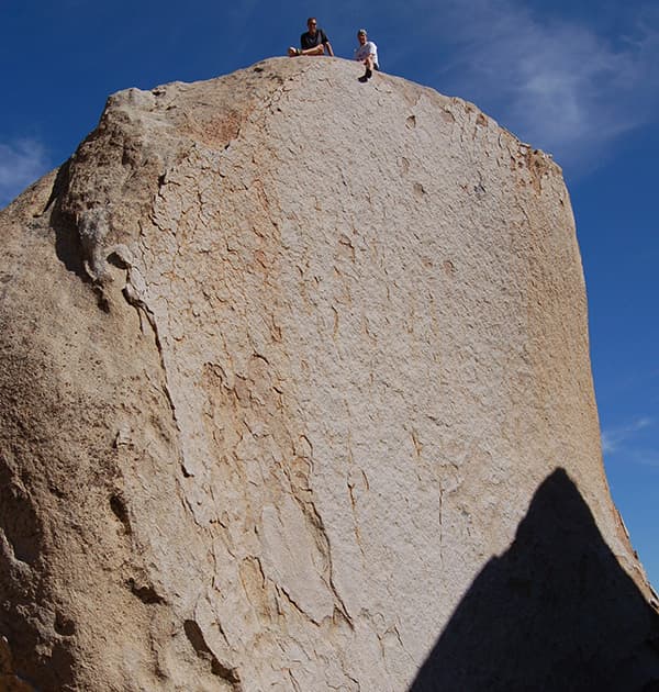 Stefan Kruger and a friend sit atop a massive rock formation under a clear blue sky.