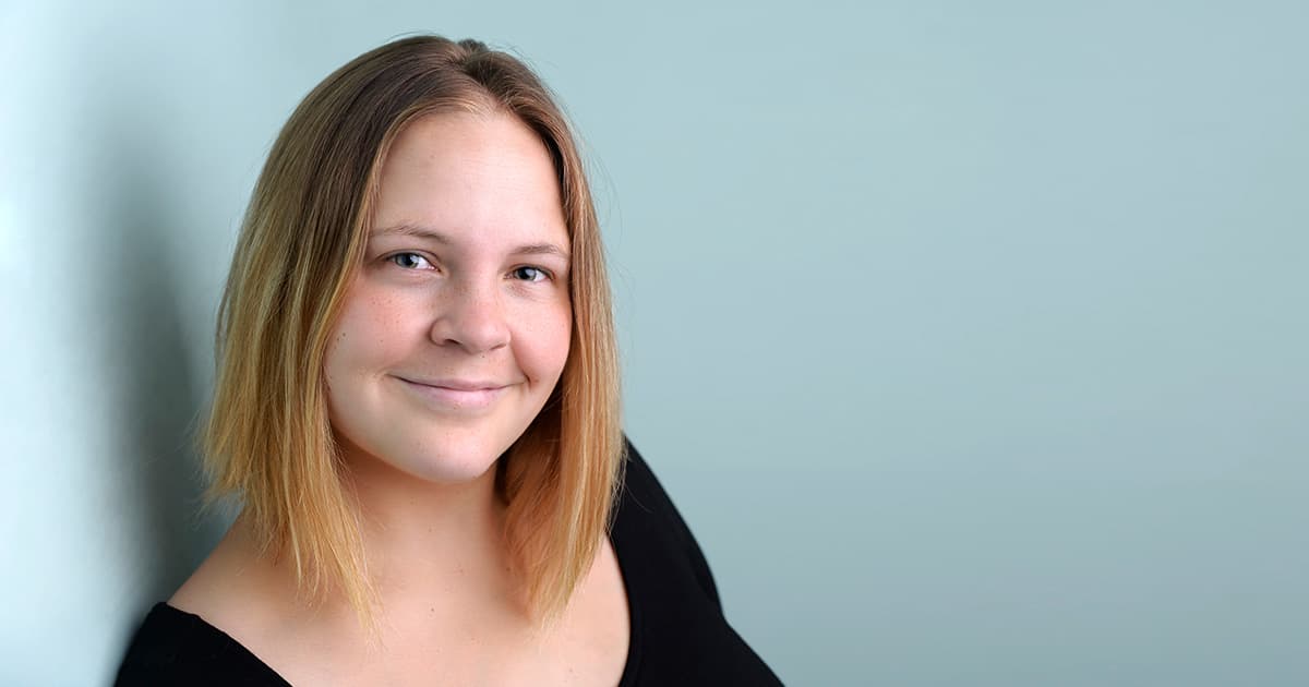 Stine Kromberg smiling softly, wearing a black top against a pale blue background.