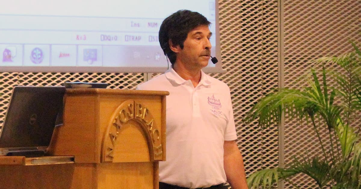 Dan Baronet wearing a Dyalog polo shirt, speaking at a podium with a microphone headset during Dyalog ’15 in Sicily.