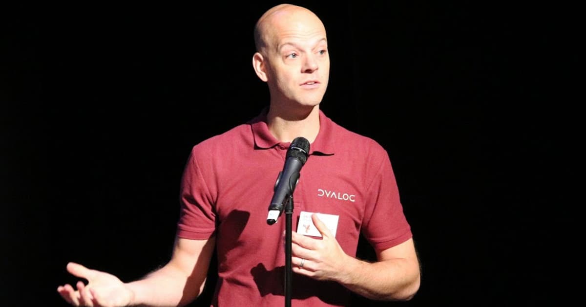 Jay Foad speaking on stage at Dyalog ’18, wearing a maroon Dyalog shirt and addressing the audience with a microphone.