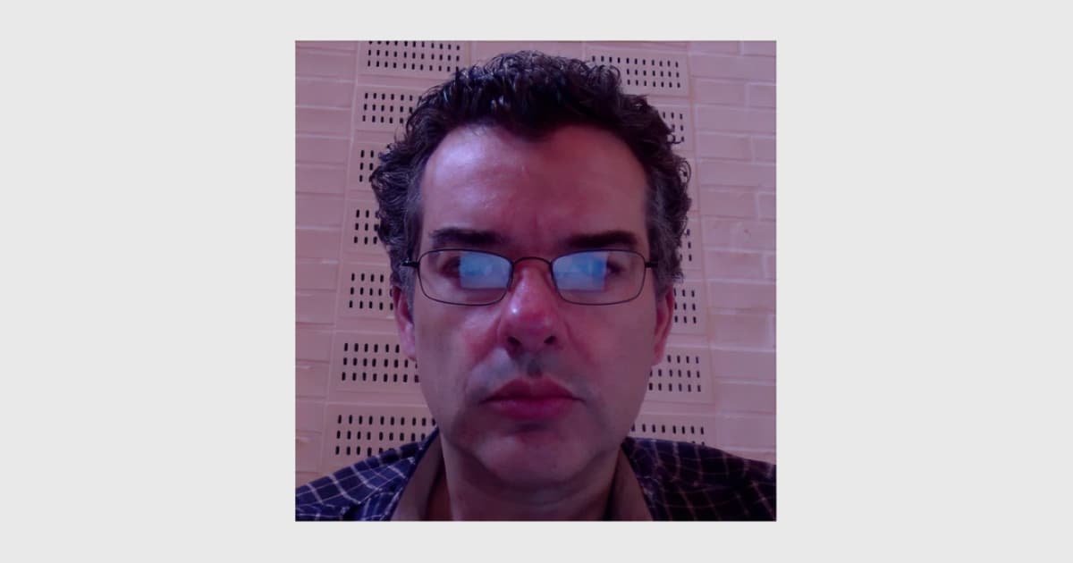 John Daintree at Dyalog ’14, looking toward the camera in a close-up portrait with a patterned wall behind him.