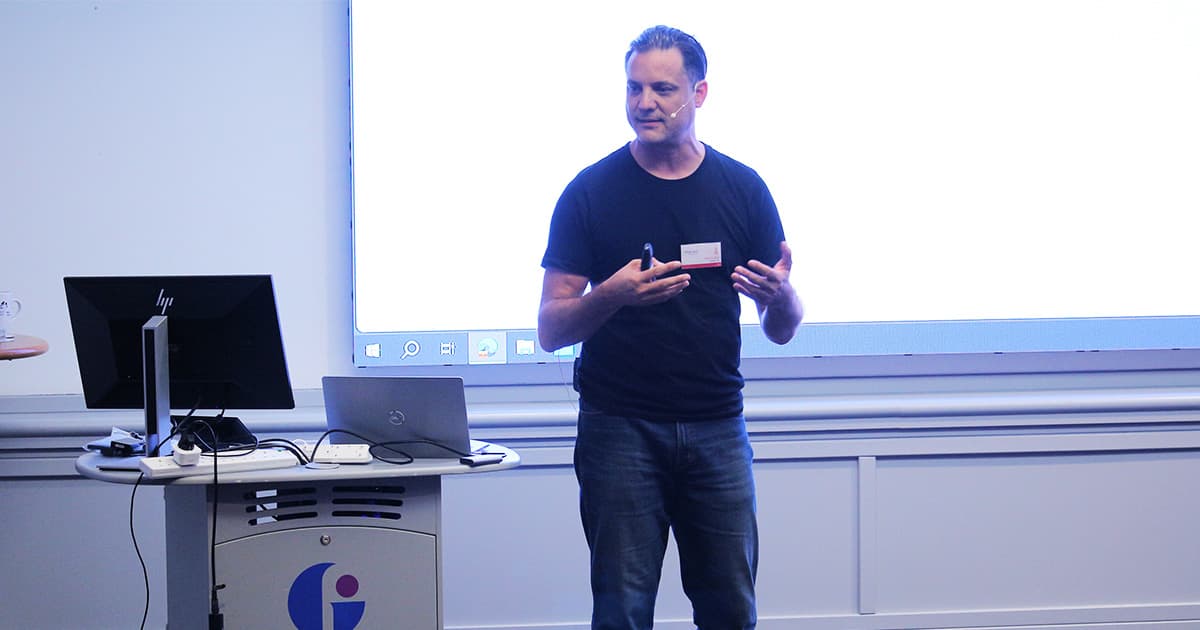 Oliver Lanz presenting at Dyalog ’24 in Glasgow. He stands in front of a projected screen, wearing a black t-shirt, gesturing with both hands while addressing the audience.