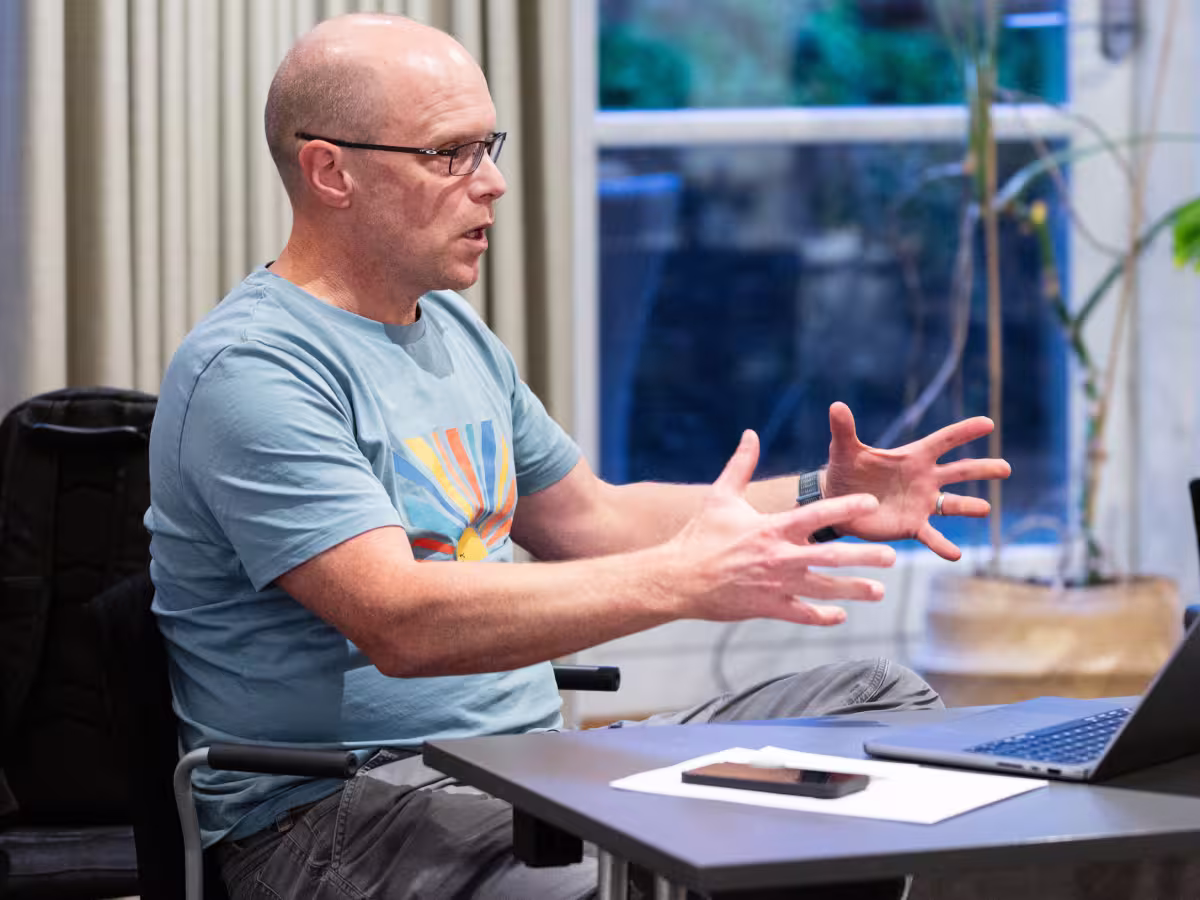 Stefan Kruger sitting at a table and gesturing while speaking, with an open laptop in front of him in an indoor meeting space.