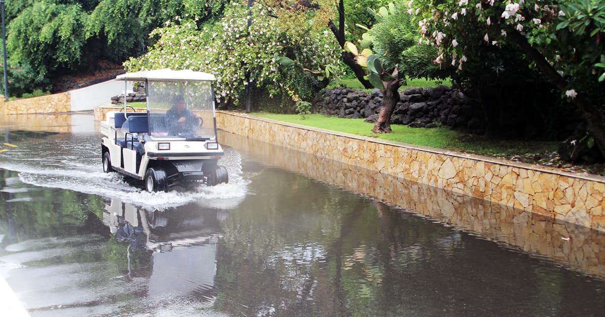 A golf cart drives through a flooded pathway lined with stone walls and lush greenery at Atahotel Naxos Beach during Dyalog '15.